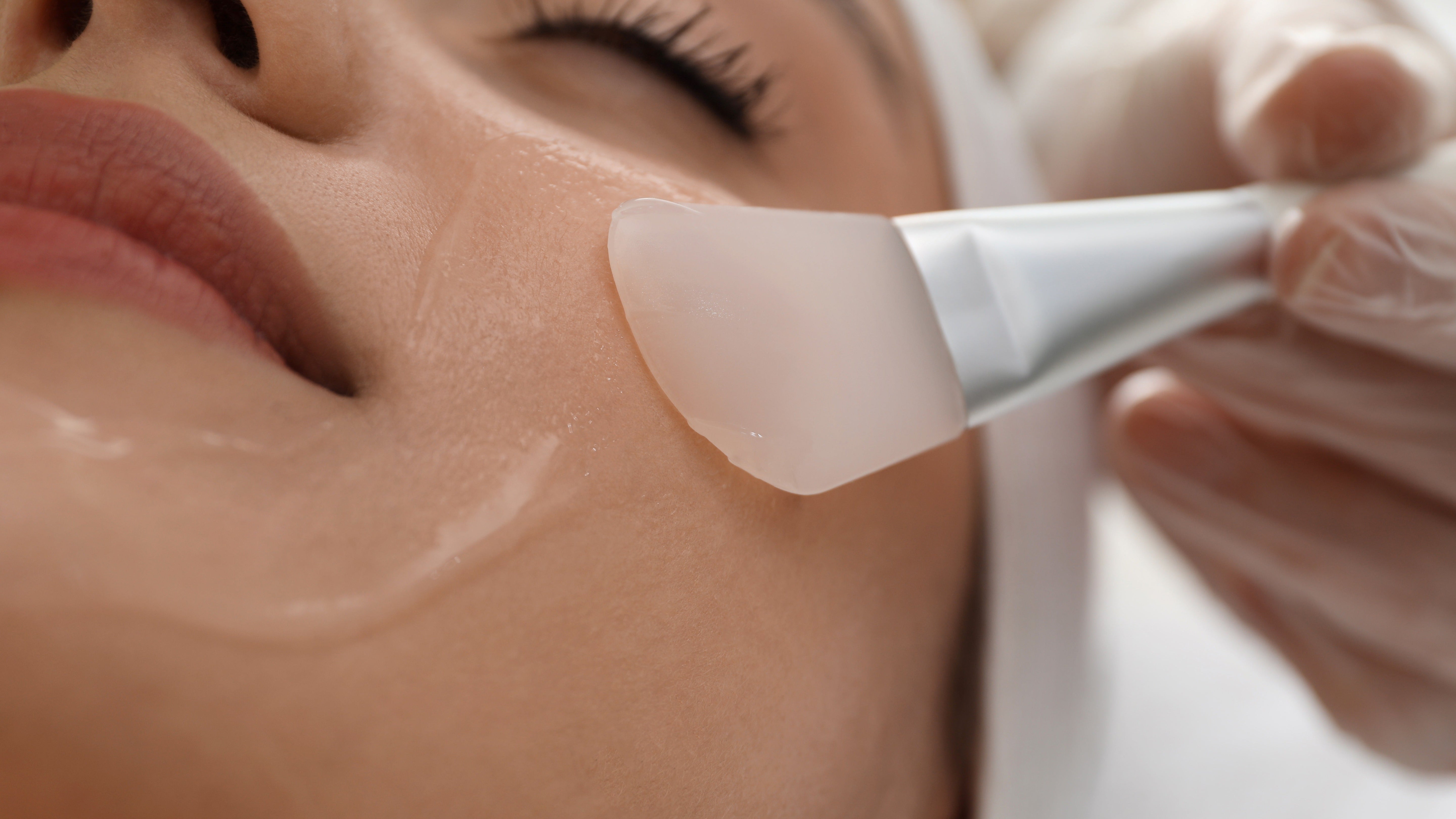Close-up of a woman receiving a facial treatment with a brush applying a chemical peel solution