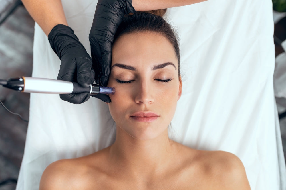 Woman receiving an exosome facial treatment from a skin therapist using a handheld device on her cheek.