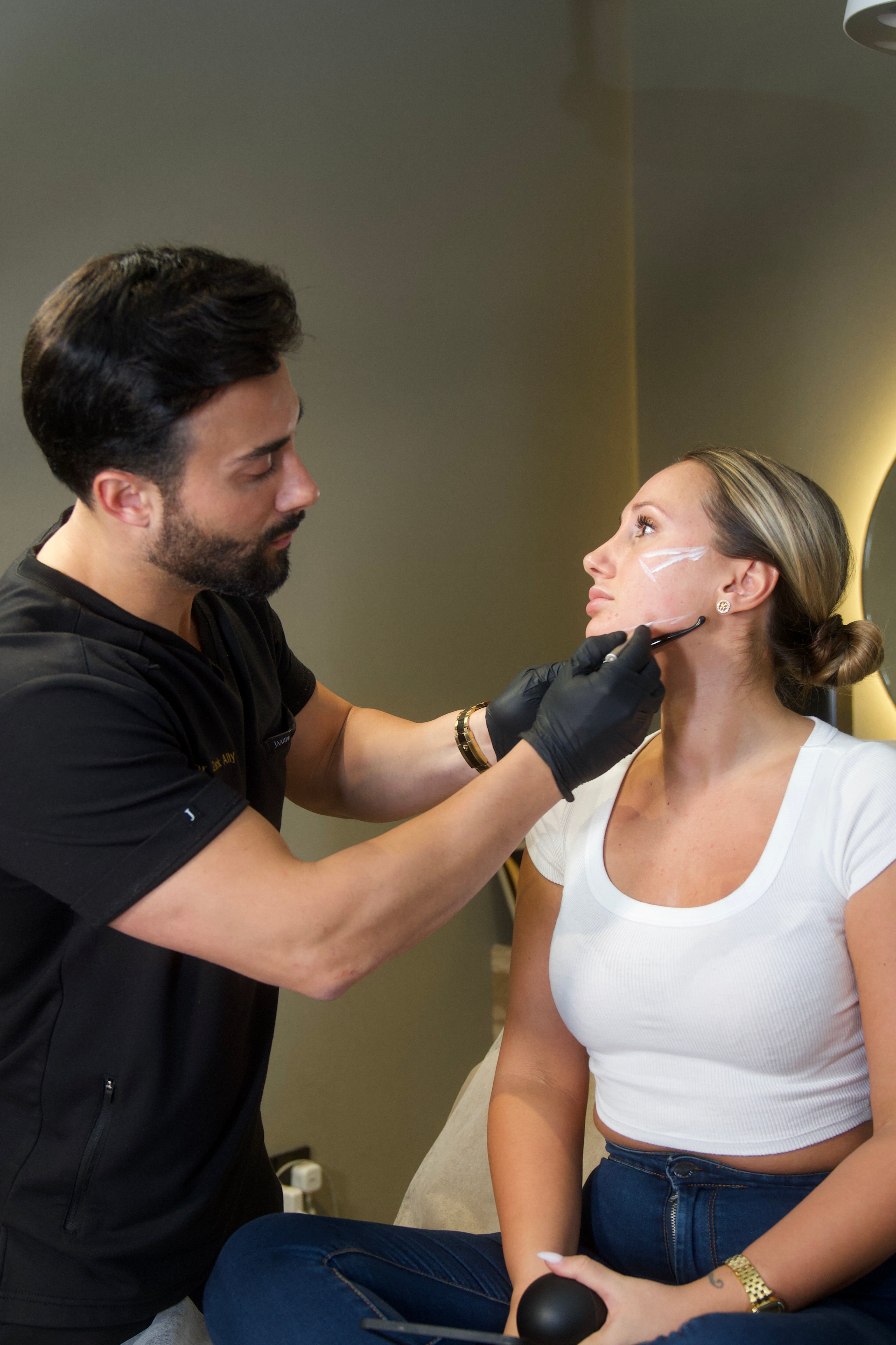 A specialist applies Radiesse treatment to a woman's face, marking injection sites on her cheek and jawline at BROWZ.