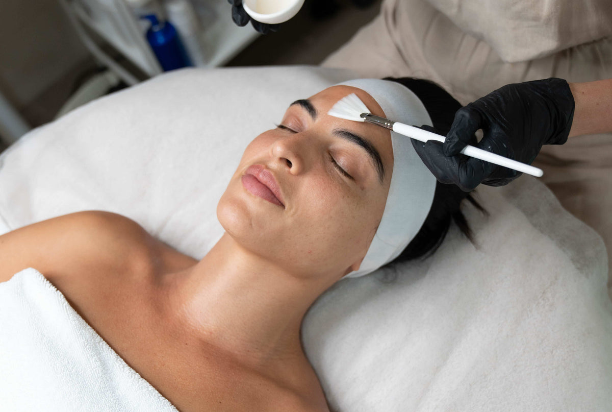 Chemical peel treatment being applied to a client’s forehead with a brush during a professional skincare procedure. 